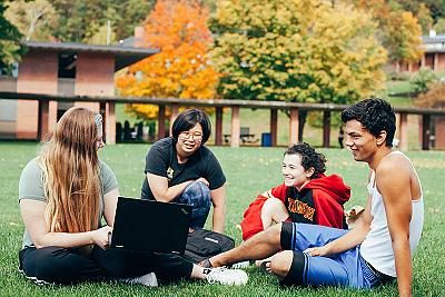  Students sitting on the grass outside of the Student Center in Autumn.